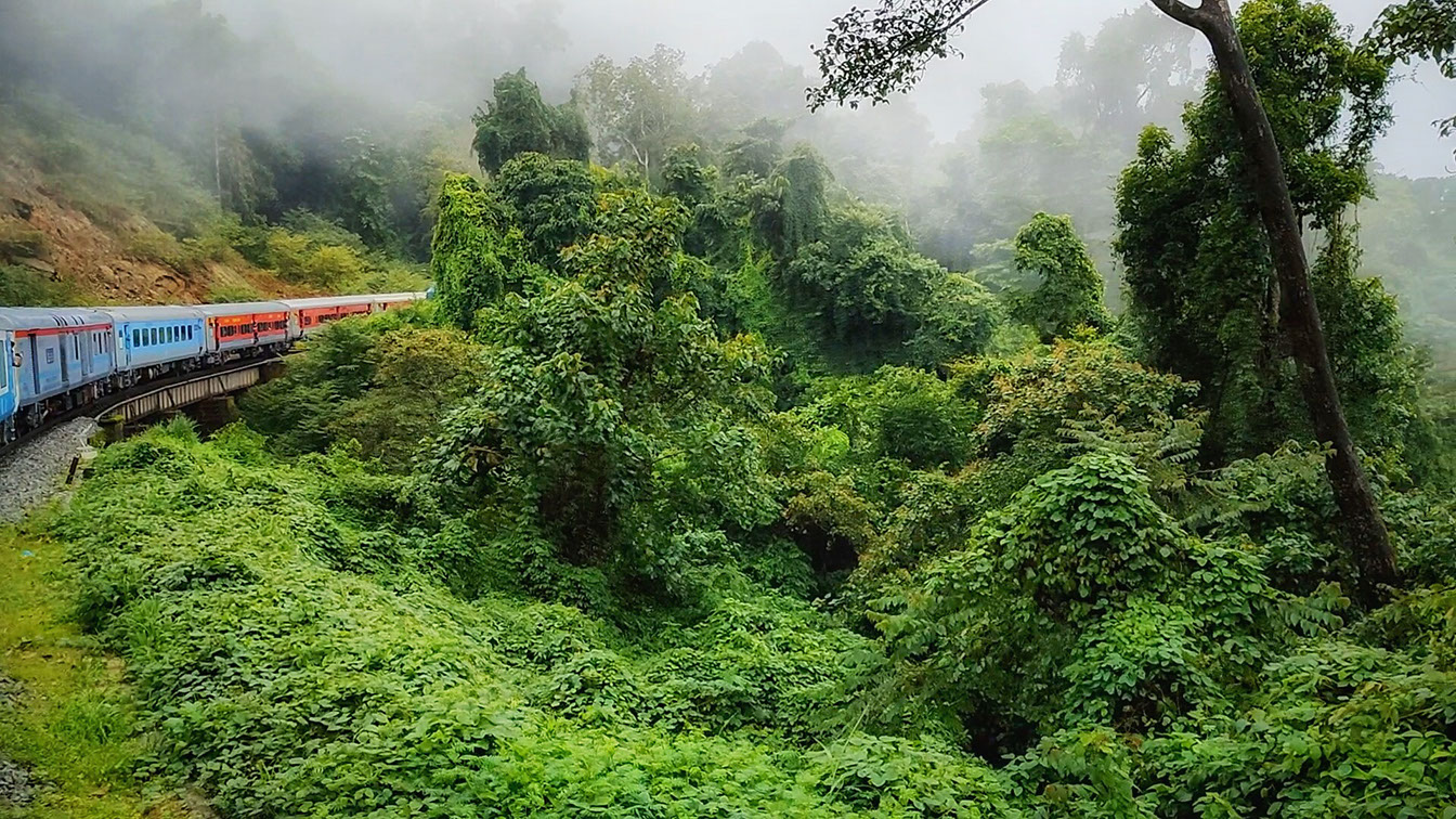 Under hazy weather, a train makes a large bend in the difficult terrain of the Western Ghats.